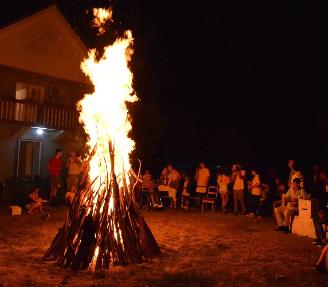 Foc de tabără seara, cu participanții adunați în jurul lui