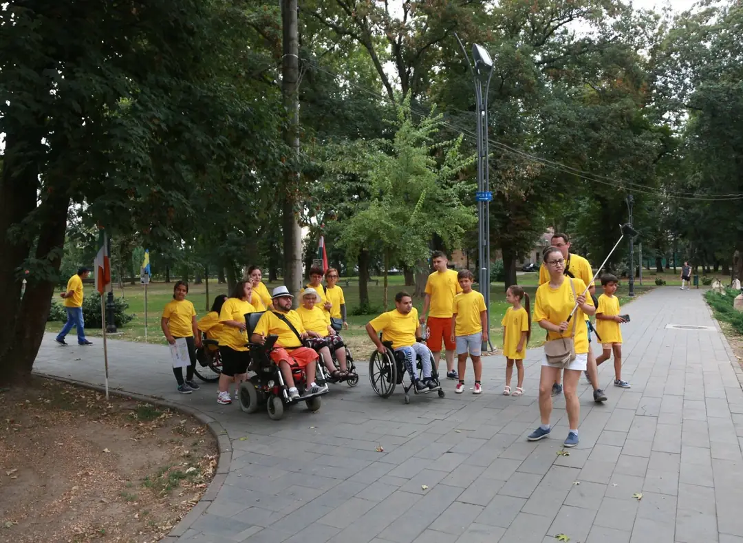 Voluntari în tricouri galbene, alături de participanți în scaune rulante, la o plimbare prin parc