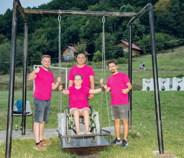 O participantă pe leagănul pentru scaune rulante, alături de trei voluntari